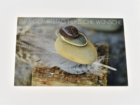 Geburtstagskarte mit einem chinesischen Sprichwort, natürlichem Hintergrund, einer Stein-Obelisken-Komposition und einer Feder, verziert mit der Aufschrift Zum Geburtstag herzliche Wünsche.