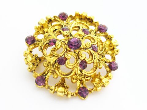 Brosche im Sexy City Look mit lila Strass, rundes Design, goldfarbene Details, Hersteller Juwelier Harnisch, ideal für elegante Akzente und besondere Anlässe.