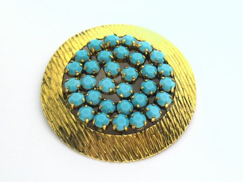 Runde Strass Brosche mit gefassten türkis look Steinen, umgeben von goldfarbigem, strukturiertem Metall, Hersteller Juwelier Harnisch, ideal für stilvolle Akzente.