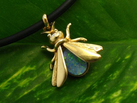 Fliege Goldanhänger mit Opal Triplette, 17mm Zweiflügler, Hersteller Juwelier Harnisch, zeigt feine Details und schimmernden Opal in goldener Fassung auf grünem Blatt.