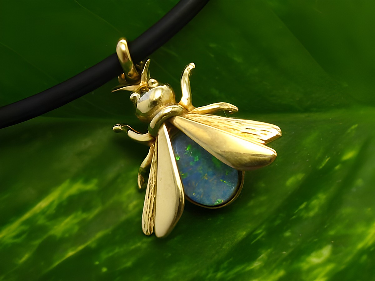 Fliege Goldanhänger mit Opal Triplette, 17mm Zweiflügler, Hersteller Juwelier Harnisch, zeigt feine Details und schimmernden Opal in goldener Fassung auf grünem Blatt.