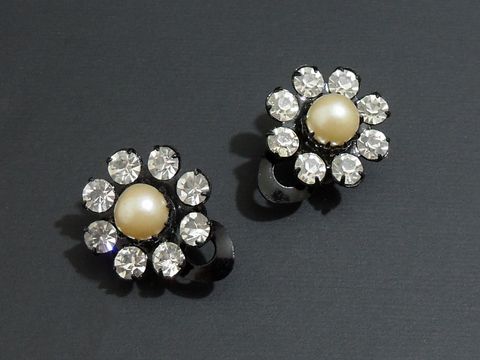 Strass Ohrclips in grazilem Design, kombiniert mit weißen und schwarzen Elementen, funkeln mit einer zentralen Perle und sind vom Hersteller Juwelier Harnisch. Ideal für elegante Anlässe.