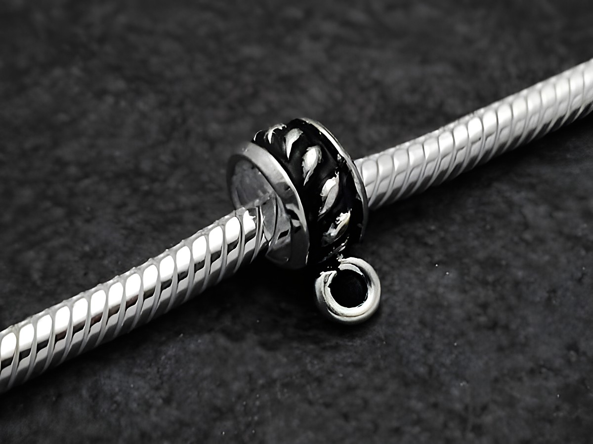 Design BLANKO charms Einhänger aus Sterling Silber mit einem Durchmesser von 4,8 mm, gefertigt vom Juwelier Harnisch, im Detail auf einem silbernen Armband präsentiert.