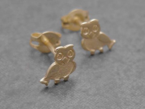 Ohrringe in Eulenform aus goldenem Metall, symbolisch für Weisheit und Schutz, hergestellt vom Juwelier Harnisch, zieren die Ohren und bringen Tierliebe zum Ausdruck.