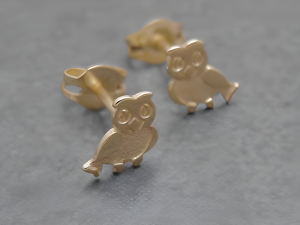 Ohrringe in Eulenform aus goldenem Metall, symbolisch für Weisheit und Schutz, hergestellt vom Juwelier Harnisch, zieren die Ohren und bringen Tierliebe zum Ausdruck.