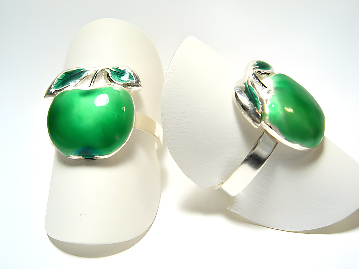 Designer Silber Ring rhodiniert -Apfel- in grün, Hersteller Juwelier Harnisch, ohne Stein, zeigt einen stilisierten grünen Apfel als Ringdesign auf einem weißen Träger.