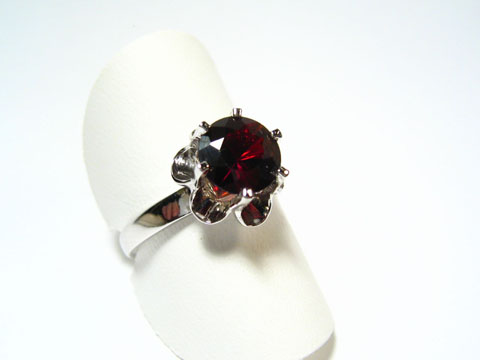Silber Ring rhodiniert mit einem rot gefassten Echt Granat, verstellbar, Hersteller Juwelier Harnisch, präsentiert auf einem weißen Ringkissen.