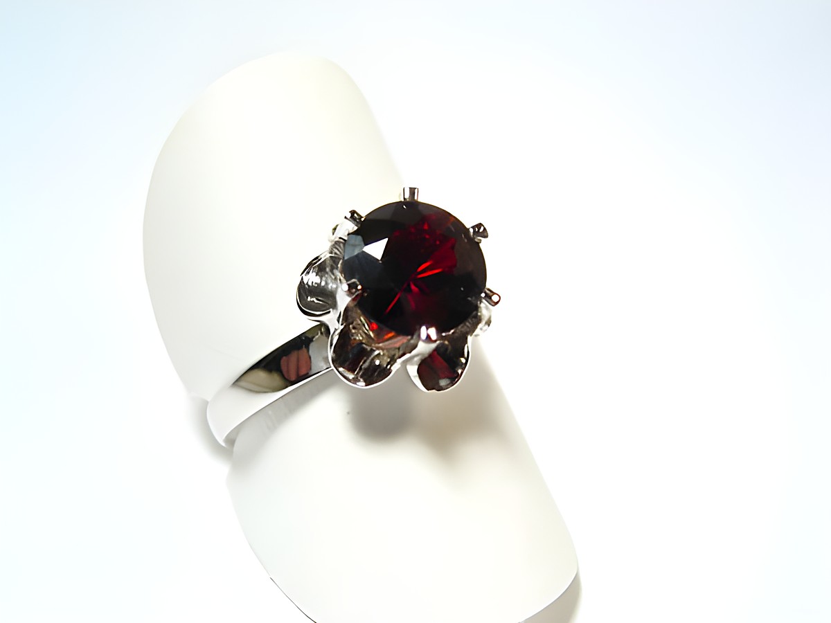 Silber Ring rhodiniert mit einem rot gefassten Echt Granat, verstellbar, Hersteller Juwelier Harnisch, präsentiert auf einem weißen Ringkissen.