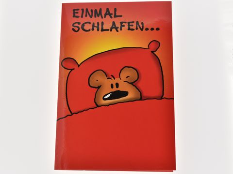 Eine rote Geburtstagskarte mit einem Bärchen, das im Bett liegt und schläfrig schaut. Der Text "EINMAL SCHLAFEN..." ist oben auf der Karte zu sehen. Hersteller ist Juwelier Harnisch.