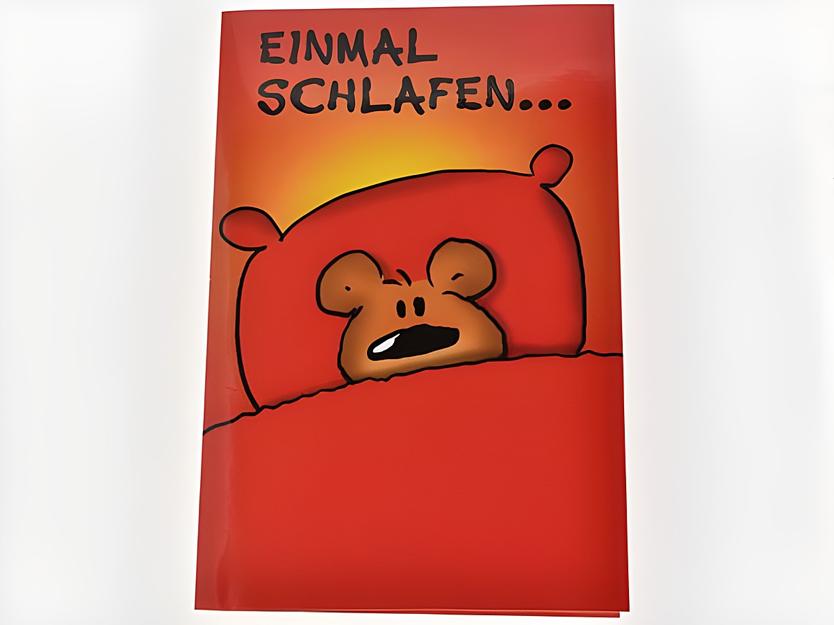 Eine rote Geburtstagskarte mit einem Bärchen, das im Bett liegt und schläfrig schaut. Der Text "EINMAL SCHLAFEN..." ist oben auf der Karte zu sehen. Hersteller ist Juwelier Harnisch.