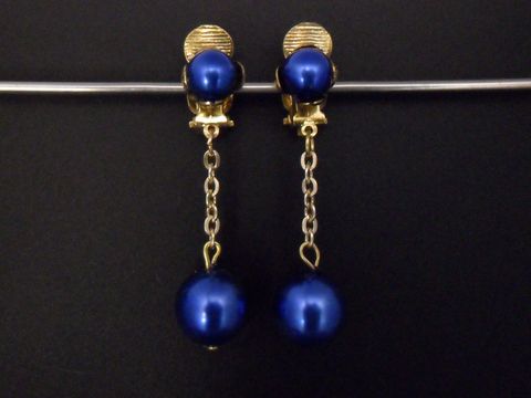 Ohrclip in blau glänzend und goldfarben aus Kunstharz, zeitloses Design mit einer längeren Kette und einer runden, blauen Perle, Hersteller: Juwelier Harnisch.