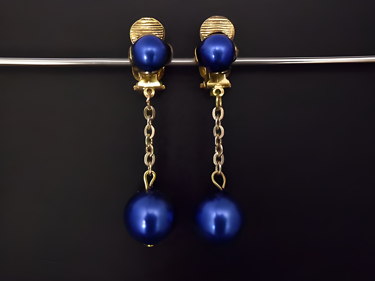 Ohrclip in blau glänzend und goldfarben aus Kunstharz, zeitloses Design mit einer längeren Kette und einer runden, blauen Perle, Hersteller: Juwelier Harnisch.