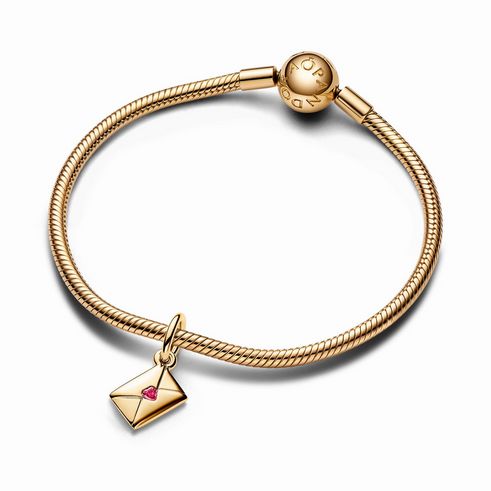 Charm-Anhänger von Pandora in Gelbgold vergoldet, gestaltet als Liebesbrief mit einem roten Zirkonia-Herzen, hängt an einem eleganten Armband. Ideal für romantische Anlässe.