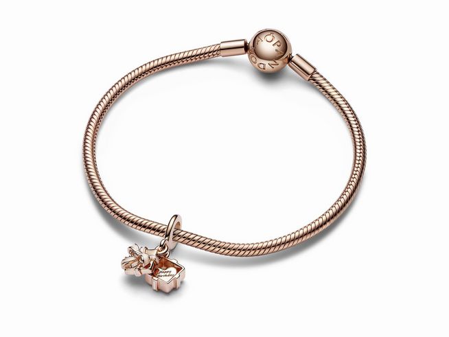 Auf dem Bild ist ein Pandora Aufklappbares Geburtstagsgeschenk Charm-Anhänger in Roségold Vergoldung und Emaille zu sehen, der an einem eleganten Armband befestigt ist.
