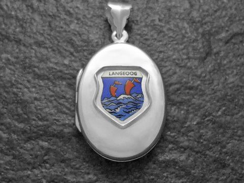 Das Bild zeigt ein silbernes Medaillon mit dem Wappen der Insel Langeoog, das einen blauen Hintergrund und rote Schiffe in bewegten Wellen darstellt, hergestellt von Juwelier Harnisch.
