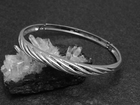 Silber Armreifen feminin 6,4 mm rhodiniert 16,5 cm von Juwelier Harnisch, elegant mit gewelltem Design auf schwarzem Hintergrund und Kristallen als Unterlage.