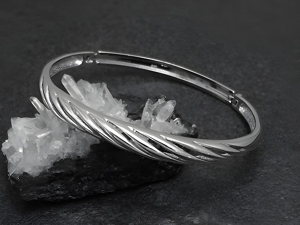 Silber Armreifen feminin 6,4 mm rhodiniert 16,5 cm von Juwelier Harnisch, elegant mit gewelltem Design auf schwarzem Hintergrund und Kristallen als Unterlage.