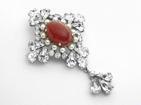Königliche Strass Brosche mit einem roten Stein und weißen Strasssteinen in elegantem Design, Hersteller Juwelier Harnisch, ideal für einen sexy City Look.