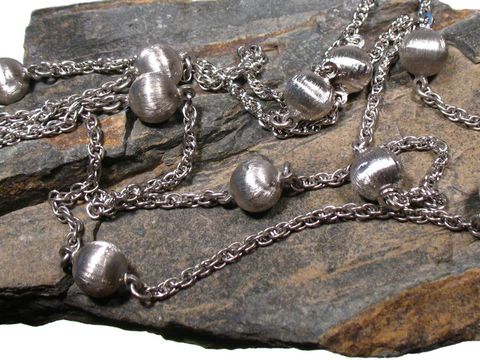 Lange Silberkette mit mattierten Perlen in rhodiniertem Design, 95 cm lang, Hersteller Juwelier Harnisch, Mittelteil der Colliers auf rustikalem Stein präsentiert.