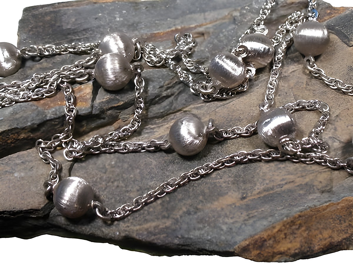Lange Silberkette mit mattierten Perlen in rhodiniertem Design, 95 cm lang, Hersteller Juwelier Harnisch, Mittelteil der Colliers auf rustikalem Stein präsentiert.