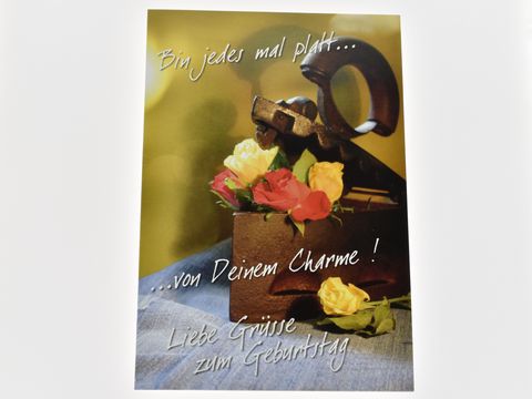Geburtstagskarte mit gelben und roten Rosen auf einer Holzfläche, unterstützt von einer stilvollen Dekoration. Hersteller Juwelier Harnisch, ideale Grüße zum Geburtstag.
