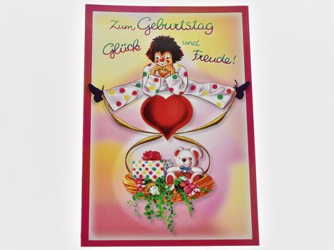 Bunte Geburtstagskarte mit einem fröhlichen Clown, der ein großes rotes Herz hält, umgeben von einem Präsentkorb mit Geschenken und einem kleinen Teddybären, Hersteller Juwelier Harnisch.