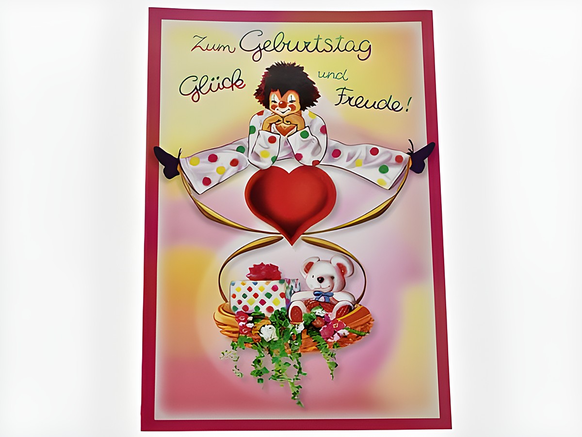 Bunte Geburtstagskarte mit einem fröhlichen Clown, der ein großes rotes Herz hält, umgeben von einem Präsentkorb mit Geschenken und einem kleinen Teddybären, Hersteller Juwelier Harnisch.
