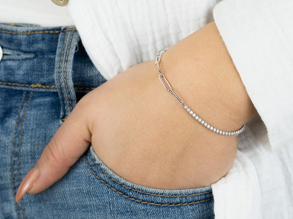 Silbernes Engelsrufer Armband mit Zirkonia, elegant am Handgelenk getragen, kombiniert moderne Ketten- und Glitzerelemente, ideal für stilvolle Anlässe und lässige Outfits.