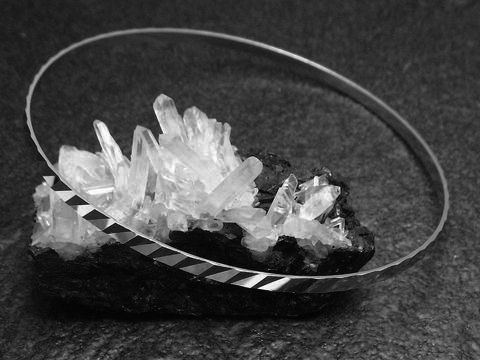 Silber Armreifen rhodiniert im 70er Schliff, 2,5 mm dick, 21 cm lang, hergestellt von Juwelier Harnisch, elegant präsentiert auf einer Kristallbasis.