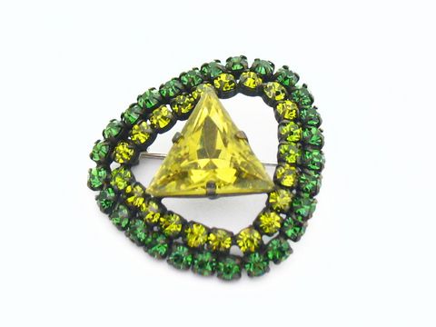 Strass Brosche Oval Grün und Gefasst, neu vom Hersteller Juwelier Harnisch, mit einem gelben, dreieckigen Kristall in der Mitte, umgeben von grünen Strasssteinen.