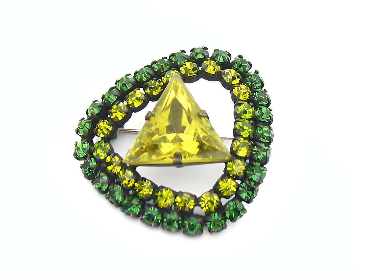 Strass Brosche Oval Grün und Gefasst, neu vom Hersteller Juwelier Harnisch, mit einem gelben, dreieckigen Kristall in der Mitte, umgeben von grünen Strasssteinen.