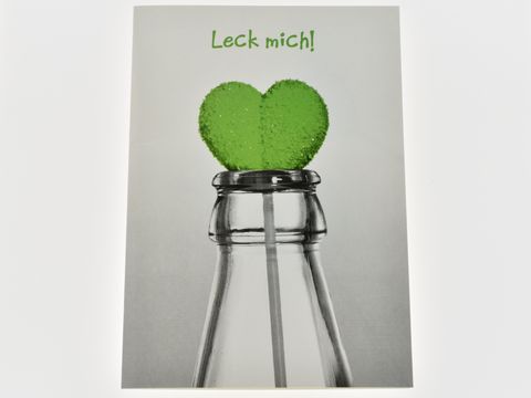 Geburtstagskarte mit einem grünen Herzlolli, der aus einer Flasche ragt. Die Karte zeigt eine auffällige Gestaltung mit der Aufschrift Leck mich. Hersteller Juwelier Harnisch.