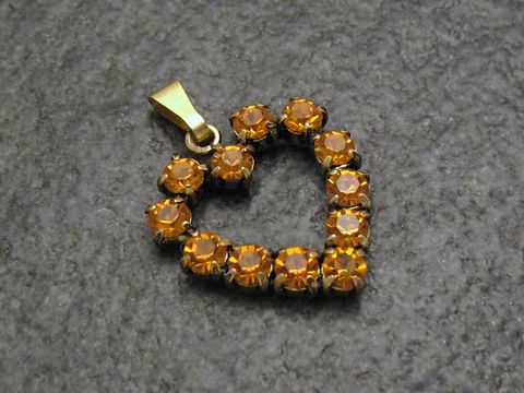 Gelber Strass Anhänger im sexy City Look in Herzform mit goldfarbener Öse, hergestellt von Juwelier Harnisch, verziert mit funkelnden orangen Strasssteinen.