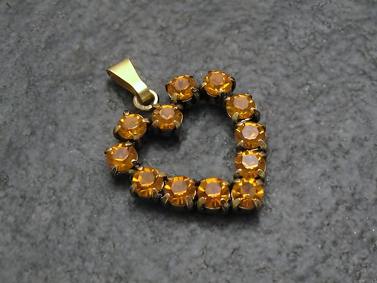 Gelber Strass Anhänger im sexy City Look in Herzform mit goldfarbener Öse, hergestellt von Juwelier Harnisch, verziert mit funkelnden orangen Strasssteinen.
