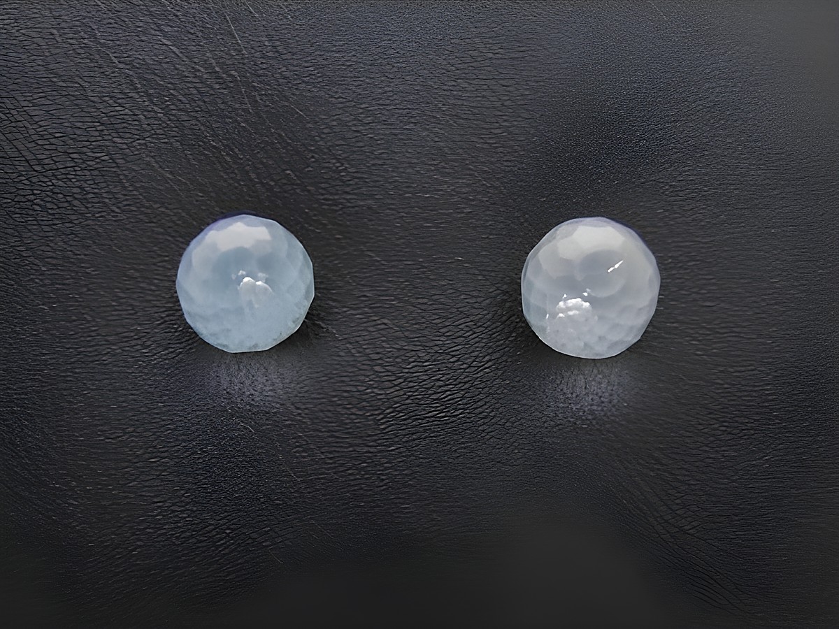 Zwei facettierte Blautopas Ohrstecker aus Sterling Silber in Kugel-Design, hergestellt von Juwelier Harnisch, auf schwarzem Hintergrund platziert.