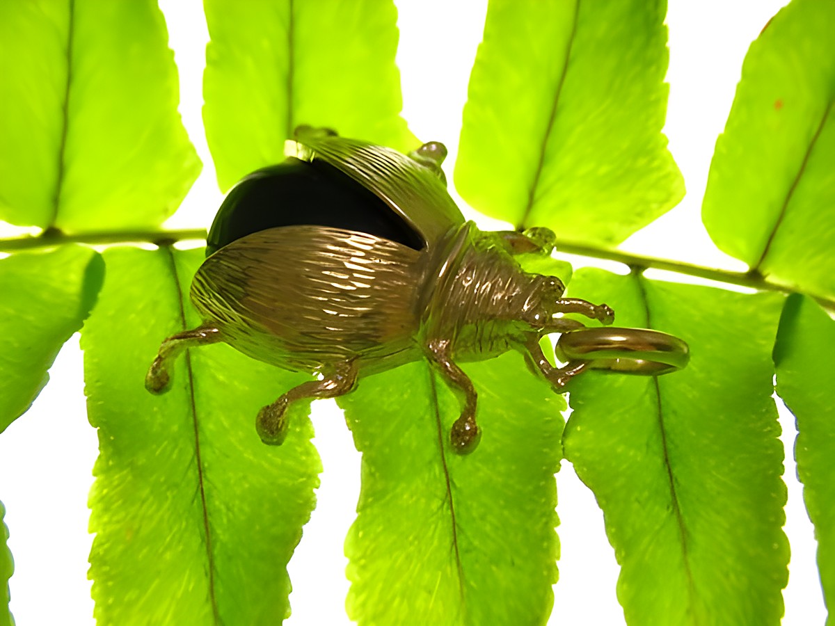Käfer Coleoptera Goldanhänger aus Gold und Onyx auf einem Blatt. Hersteller Juwelier Harnisch. Detailreiche Darstellung des Anhängers mit natürlichem Hintergrund.