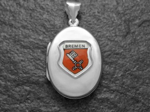 600007201-0 Ein silbernes Medaillon mit dem Wappen von Bremen, das ein orangefarbenes Schild zeigt. Das Wappen enthält die Inschrift Bremen und emblematische Symbole. Hersteller ist Juwelier Harnisch aus Bremen.