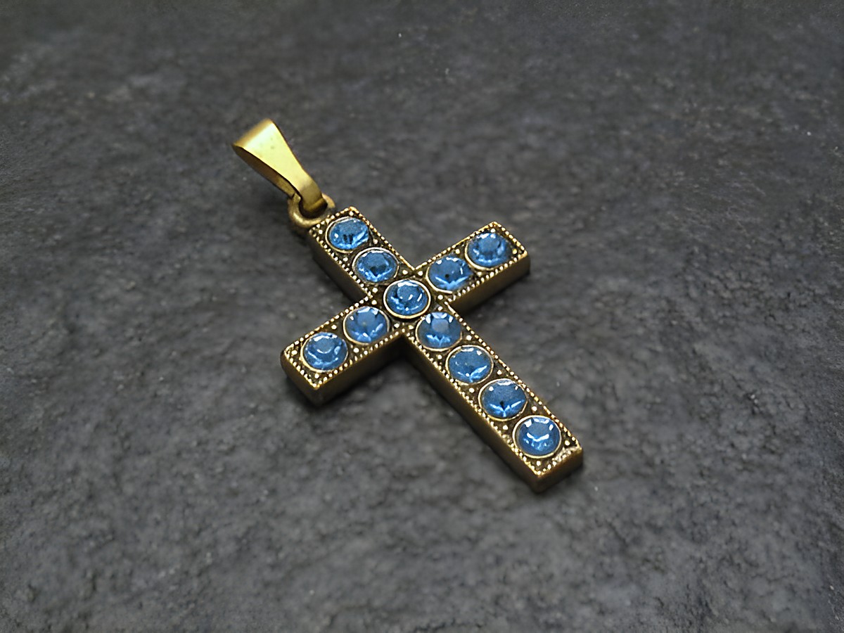 Blauer Strass Anhänger im sexy City Look in Form eines Kreuzes, Hersteller Juwelier Harnisch, verziert mit funkelnden blauen Strasssteinen auf einem eleganten goldfarbenen Hintergrund.