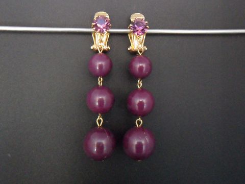 Ohrclip in lila mit drei Kunstharzkugeln und goldfarbener Fassung, verziert mit einem lila Stein, hergestellt von Juwelier Harnisch. Zeitloses Design für jede Gelegenheit.