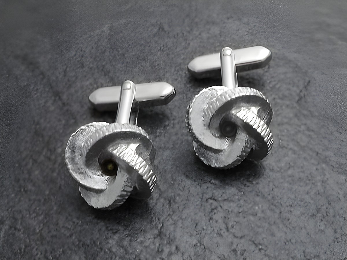Manschettenknöpfe silberfarben im Design einer Knotenform, Hersteller Juwelier Harnisch, goldfarbenes Detail, elegant und stilvoll, ideal für besondere Anlässe.
