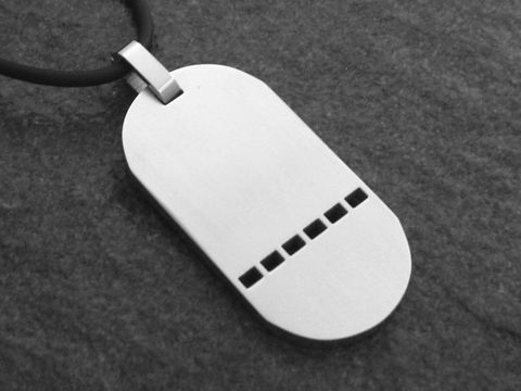 Edelstahl Anhänger mit einer Größe von 42 mm, schlichtes Design mit einer Gravurplatte und fünf vertikalen Einkerbungen, angebracht an einem schwarzen Halsband, Hersteller Juwelier Harnisch.