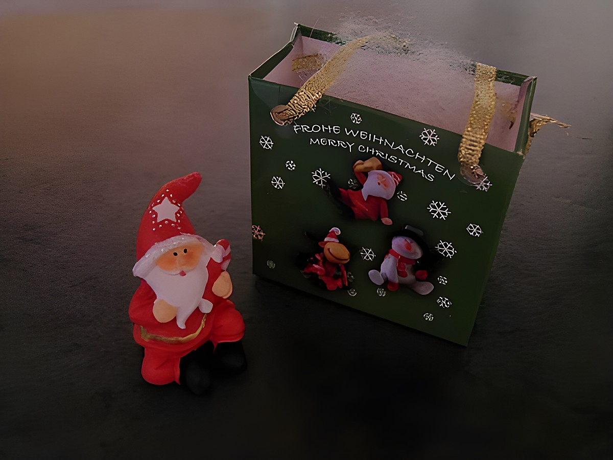 Weihnachtsmann mit Geschenktasche sitzend, hält eine Zuckerstange in der Hand, neben einer grünen Geschenktüte mit festlichem Design von Juwelier Harnisch, für Weihnachten.