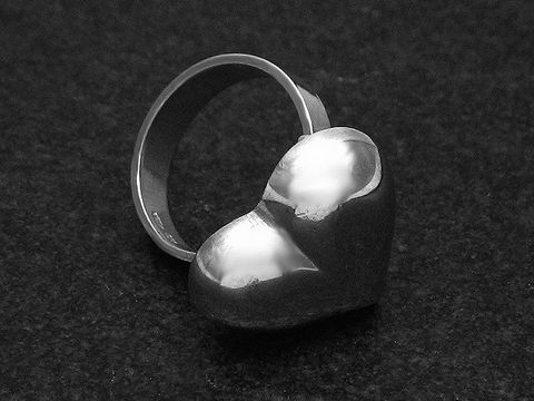 Silberring in Herzform, plastisch gestaltet, Größe weit verstellbar, Hersteller Juwelier Harnisch, ohne Stein, auf schwarzem Hintergrund.