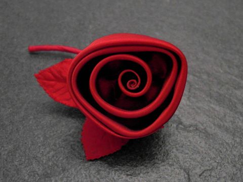 Haarschmuck in Form einer roten Satinrose mit zarten Blättern, ideal als Brosche von Juwelier Harnisch, verleiht jedem Outfit floralen Charme.