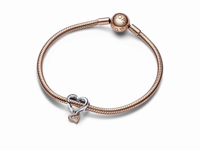 Bicolor Unendlichkeit Herz Charm von Pandora aus Sterling Silber und Roségold Vergoldung, an einem feinen Armband befestigt, elegant und zeitlos gestaltet.
