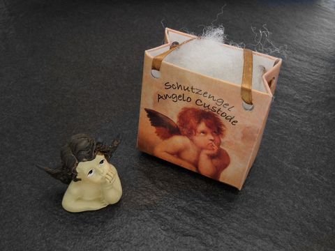 Brauner Schutzengel mit Geschenktasche, nachdenklich, Hersteller Juwelier Harnisch, ideal für Weihnachten. Der Engel wirkt besinnlich und harmonisch neben der festlichen Verpackung.