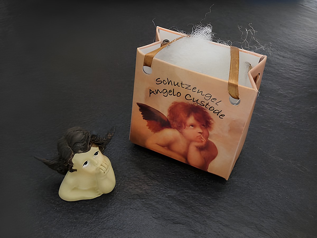 Brauner Schutzengel mit Geschenktasche, nachdenklich, Hersteller Juwelier Harnisch, ideal für Weihnachten. Der Engel wirkt besinnlich und harmonisch neben der festlichen Verpackung.