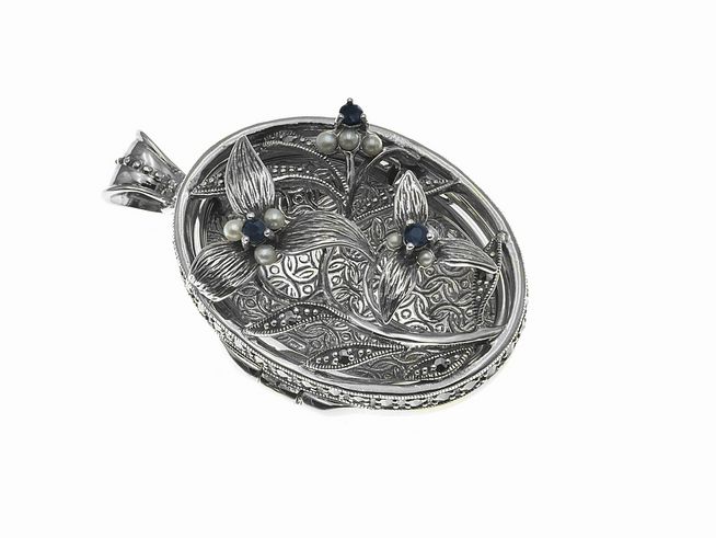 Ein nostalgisch königliches Medaillon aus Sterling Silber, oval geformt, verziert mit floralen Motiven und blauen sowie weißen Perlen, hergestellt von Juwelier Harnisch.