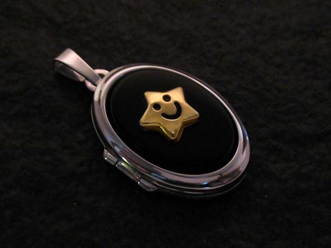 Medaillon aus Weißgold 585 mit Cabochon in Schwarz, verziert mit einem goldenen Stern und einem lächelnden Gesicht, hergestellt von Juwelier Harnisch.