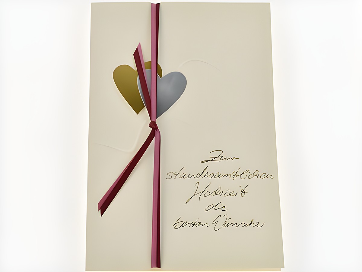 Hochzeitskarte aus strukturiertem Papier in Beige mit goldenen und silbernen Herzen, verziert mit einem roten Band. Hersteller ist Juwelier Harnisch. Ideal für Hochzeitsglückwünsche.